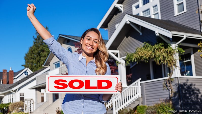 Girl holding sold sign in front of house